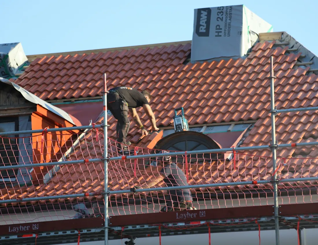 Couvreur au travail sur une toiture en tuiles, échafaudage en place