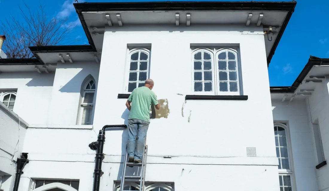 Peintre sur une échelle repeignant une façade